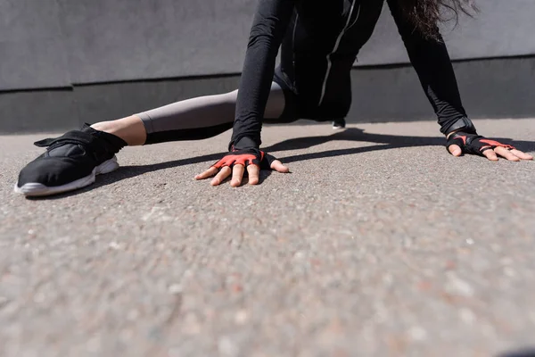 Cropped view of young sportswoman stretching on asphalt — Stock Photo