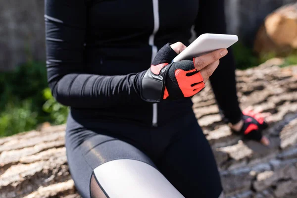 Cropped view of sportswoman holding smartphone while sitting outside — Stock Photo