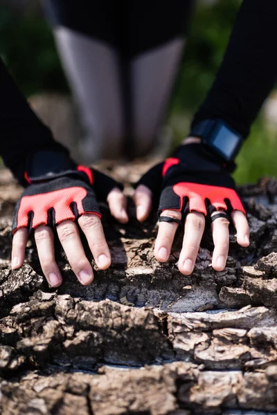 Cropped view of sportswoman in sport gloves touching tree trunk — Stock Photo