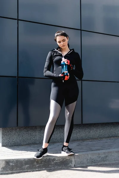 Молода жінка в чорному спортивному одязі тримає спортивну пляшку з водою — стокове фото