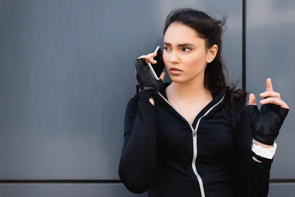 Young sportswoman looking away and gesturing while talking on smartphone — Stock Photo