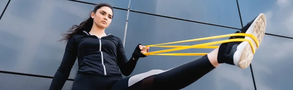 Panoramic concept of flexible young sportswoman exercising with resistance band — Stock Photo