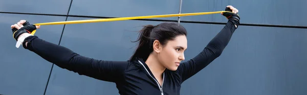 Panoramic shot of young sportswoman exercising with resistance band — Stock Photo