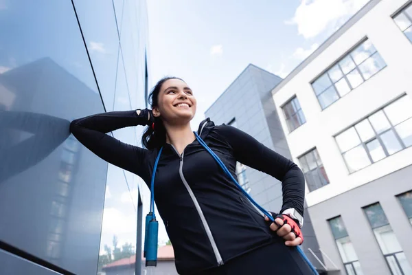 Vue à angle bas de la sportive heureuse avec corde sautante souriant à l'extérieur — Photo de stock