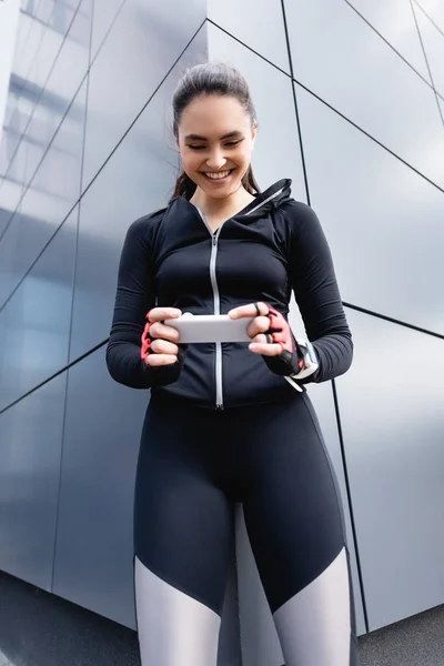 Вибірковий фокус щасливої жінки в спортивному одязі, що тримає смартфон — стокове фото