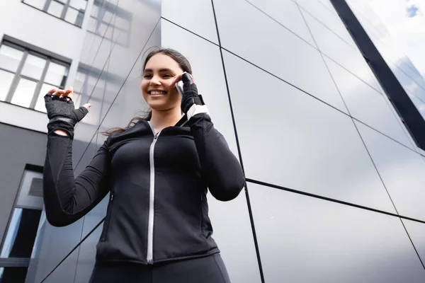 Low angle view of positive sportswoman in sportswear talking on smartphone — Stock Photo