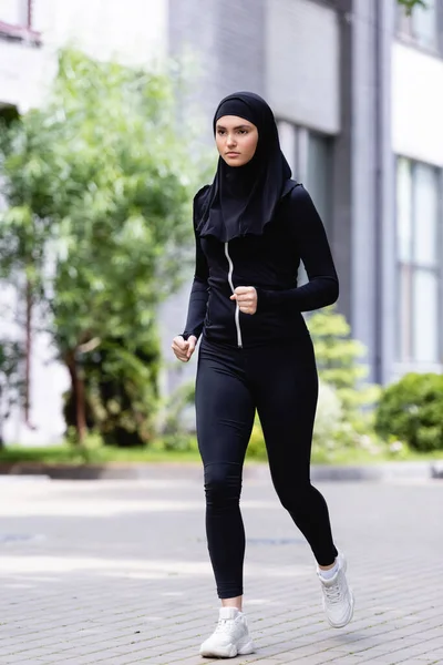 Young arabian sportswoman in hijab and sportswear running outside — Stock Photo