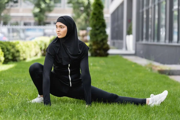 Гибкая арабская женщина в хиджабе и спортивной одежде, растянувшись на зеленой траве — стоковое фото