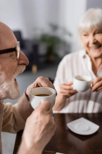 Foco seletivo de casal sênior positivo beber café na cozinha — Fotografia de Stock