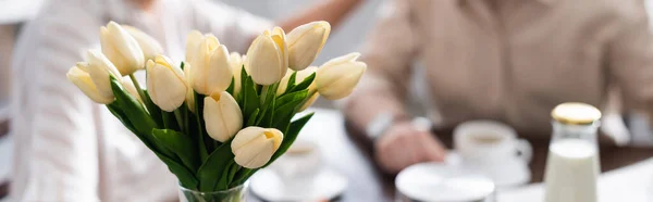 Panoramic crop of tulips in vase and senior couple drinking coffee at background — Stock Photo