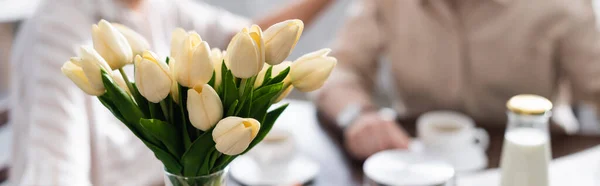 Récolte panoramique de tulipes dans un vase et couple de personnes âgées buvant du café à l'arrière-plan — Photo de stock