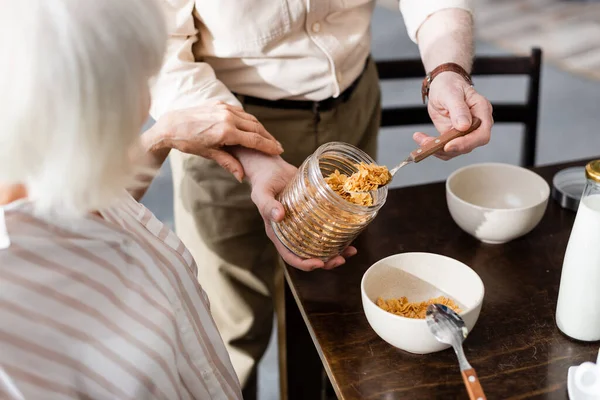 Selective focus of senior woman touching hands of husband pouring cereals in bowl — Stock Photo