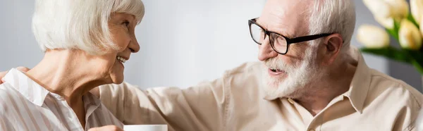 Panoramaorientierung eines lächelnden senor Mannes, der seine Frau mit einer Tasse Kaffee umarmt — Stockfoto