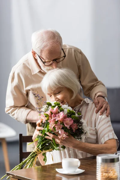 Concentration sélective de l'homme âgé embrasser femme bouquet odeur près de tasse de café sur la table — Photo de stock