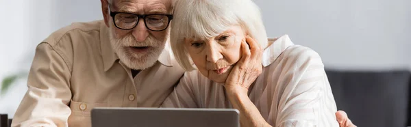 Récolte panoramique de couples âgés à l'aide d'un ordinateur portable à la maison — Photo de stock