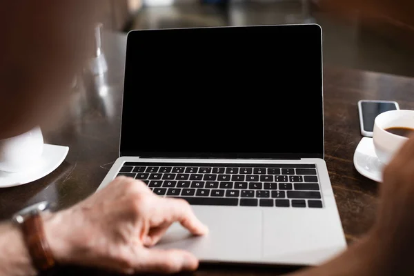 Focus selettivo della coppia anziana utilizzando laptop vicino a caffè e smartphone sul tavolo — Stock Photo