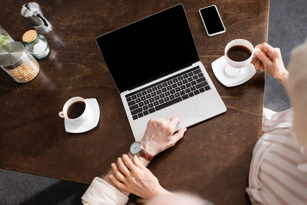 Vue aérienne de la femme âgée touchant mari à l'aide d'un ordinateur portable près du café et smartphone sur la table — Photo de stock