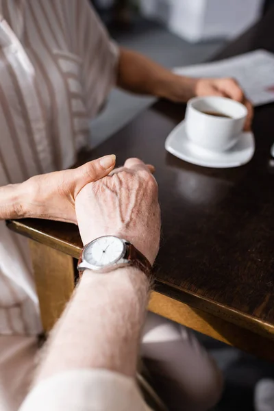 Cropped view of senior couple holding hands while drinking coffee at home — Stock Photo