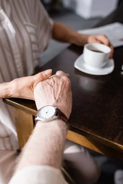 Vista recortada de la pareja de ancianos tomados de la mano mientras beben café en casa — Stock Photo