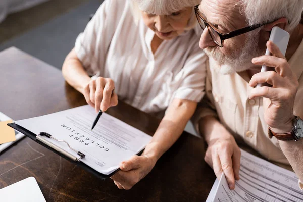 High angle view of senior man talking on smartphone near wife pointing at document with debt collection lettering — Stock Photo