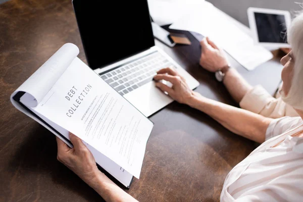 Foco seletivo da mulher usando laptop e segurando papéis com cobrança de dívidas lettering perto do homem na mesa — Fotografia de Stock