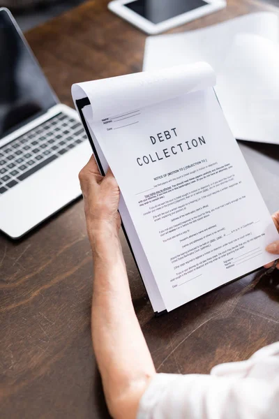 Cropped view of senior woman holding papers with debt collection lettering near digital devices on table — Stock Photo