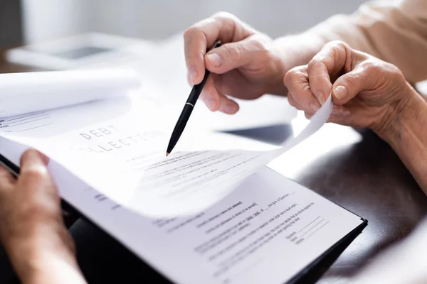 Cropped view of elderly couple holding pen and documents with debt collection lettering at home — Stock Photo