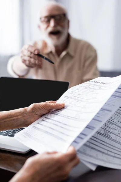 Selective focus of woman holding documents near laptop and husband pointing with pen at home — Stock Photo