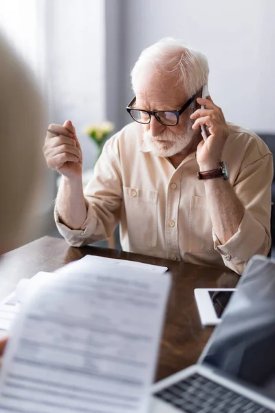 Selective focus of man talking on smartphone near papers and gadgets on table — Stock Photo