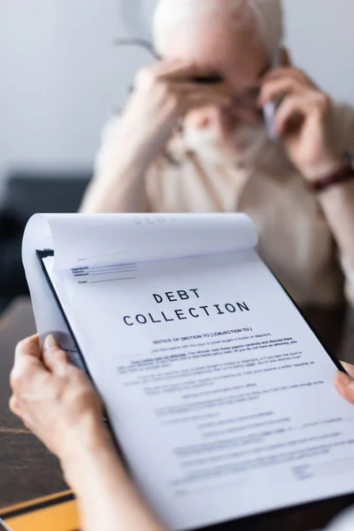 Selective focus of woman holding papers with debt collection lettering near husband talking on smartphone — Stock Photo