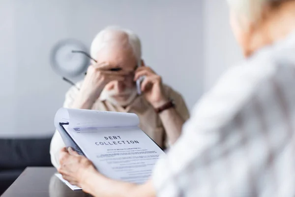 Selective focus of woman holding documents with debt collection lettering while sad husband talking on smartphone — Stock Photo