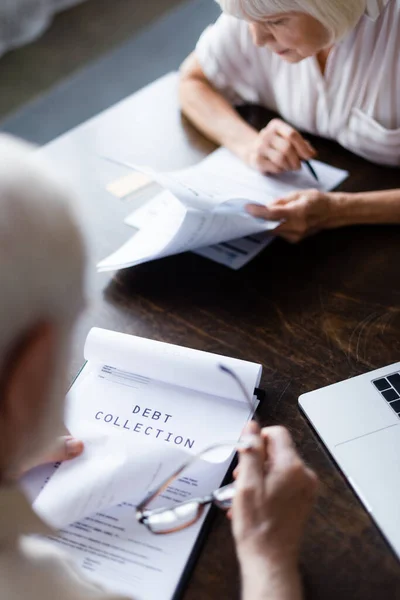 Selective focus of elderly couple looking at papers with debt collection near laptop on table — Stock Photo