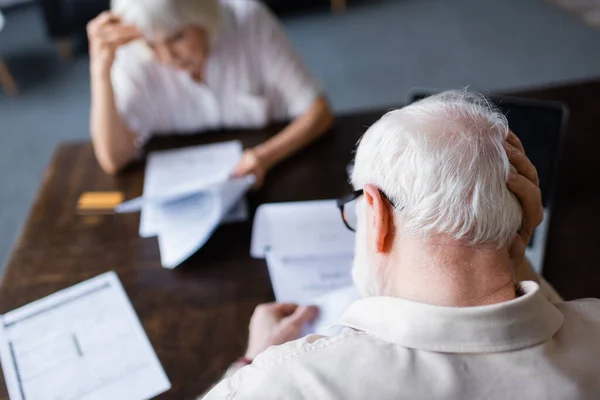 Selective focus of elderly man with hand near head holding papers near wife at home — Stock Photo