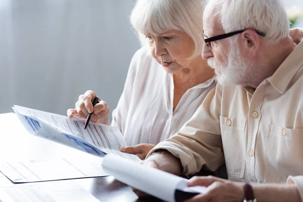 Enfoque selectivo de pareja de ancianos sosteniendo papeles en la mesa - foto de stock