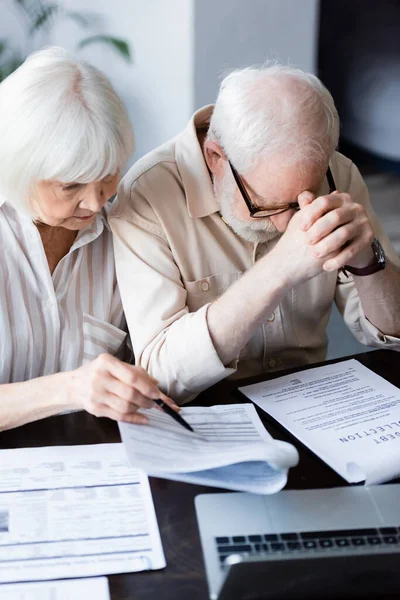 Selective focus of senior woman pointing at documents near sad husband looking at paper with debt collection lettering — Stock Photo