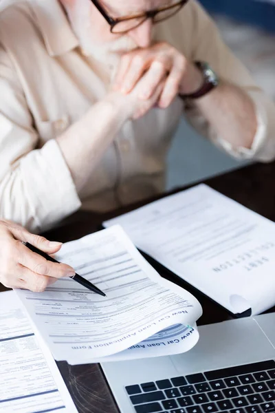 Selektiver Fokus der Frau, die mit Stift in der Nähe von Papieren und Laptop neben verärgertem Senior zeigt — Stockfoto