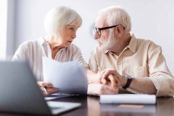 Selektiver Fokus eines älteren Ehepaares, das Hände in der Nähe von Papieren und Laptop auf dem Tisch hält — Stockfoto