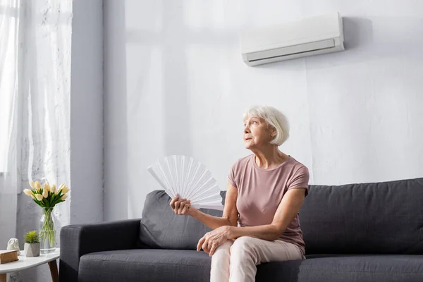 Donna anziana che tiene ventilatore mentre soffre di calore a casa — Foto stock