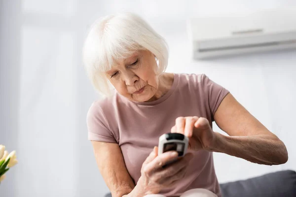 Вибірковий фокус старшої жінки за допомогою пульта дистанційного керування кондиціонером вдома — стокове фото
