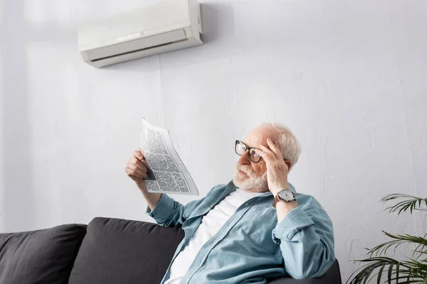 Пожилой человек держит газету на диване дома — стоковое фото