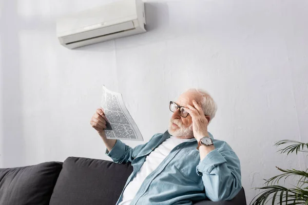 Idoso segurando jornal no sofá em casa — Fotografia de Stock