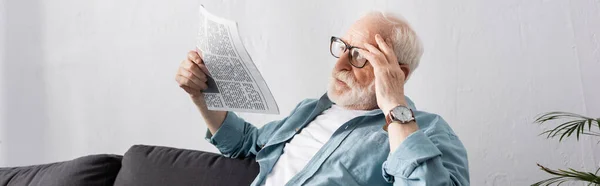 Panoramic orientation of senior man holding newspaper at home — Stock Photo