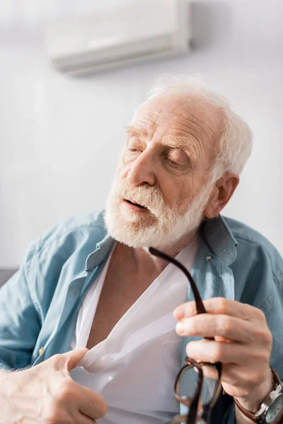 Selective focus of exhausted man holding eyeglasses and suffering from heat at home — Stock Photo