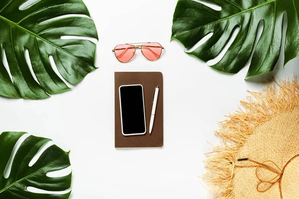 Ansicht von grünen Palmblättern, Strohhut, Sonnenbrille und Notizblock mit Smartphone auf weißem Hintergrund — Stockfoto