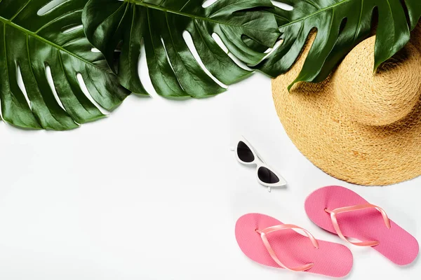 Вид сверху на зеленые пальмовые листья, соломенную шляпу, солнцезащитные очки и шлепанцы на белом фоне — стоковое фото