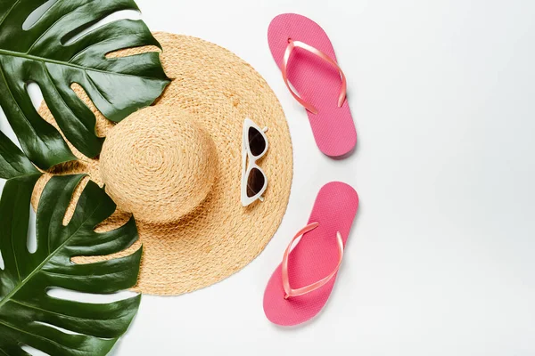 Vista superior de hojas de palma verde, sombrero de paja, gafas de sol y chanclas sobre fondo blanco - foto de stock