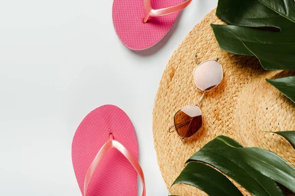 Vue du dessus des feuilles de palmier vert, chapeau de paille, lunettes de soleil et tongs sur fond blanc — Photo de stock