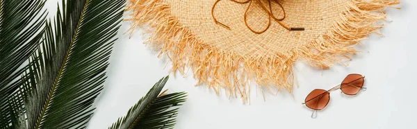 Vue de dessus des feuilles de palmier vert, chapeau de paille et lunettes de soleil sur fond blanc, vue panoramique — Photo de stock