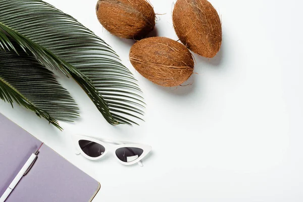 Top view of green palm leaves, sunglasses, coconuts and notepad on white background — Stock Photo