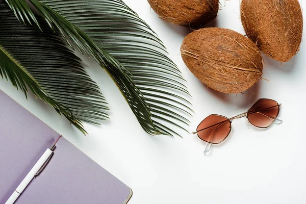 Top view of green palm leaves, sunglasses, coconuts and notepad on white background — Stock Photo